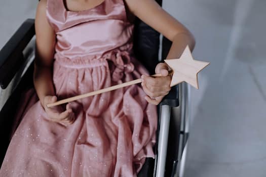 Services A child in a pink dress holding a star-shaped magic wand, seated in a wheelchair.