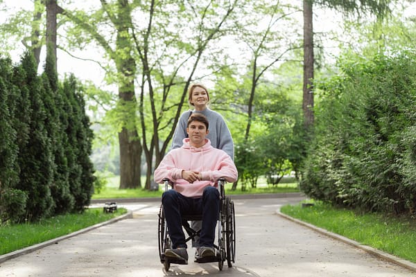 nosotros A couple enjoying a sunny day in the park, one in a wheelchair, pushing forward with a smile.
